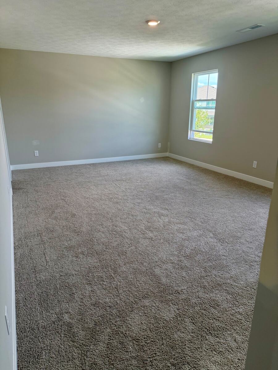 Large carpeted bedroom with recessed lighting and window