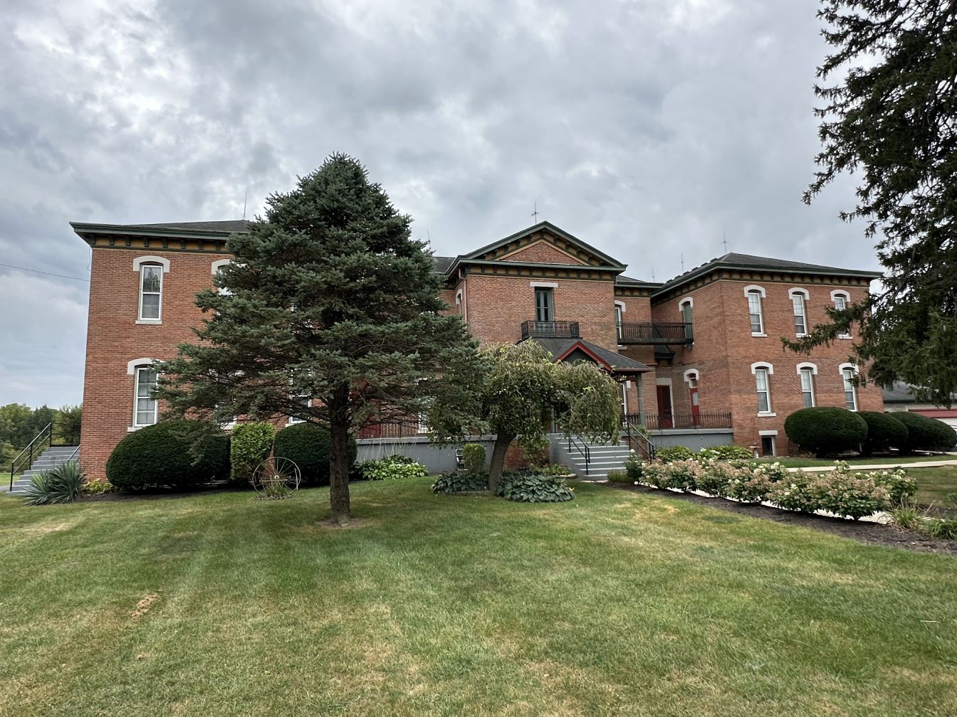 North-facing exterior of the historic Hendricks County Poor Asylum building, with mature trees and a lawn.